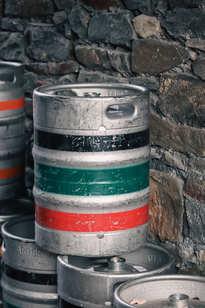 Vertical shot of stacked metal beer kegs against a rustic stone wall, showcasing brewery storage.